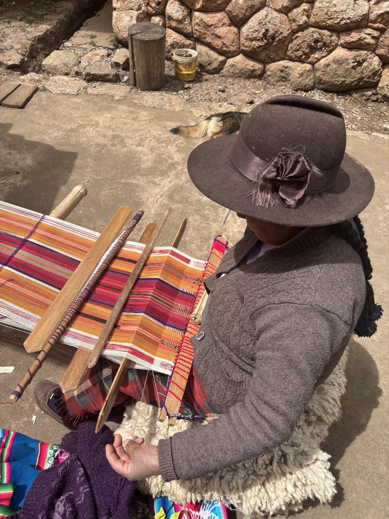 A weaver of Chinchero at her backstrap loom, working bands of orange, rose and indigo