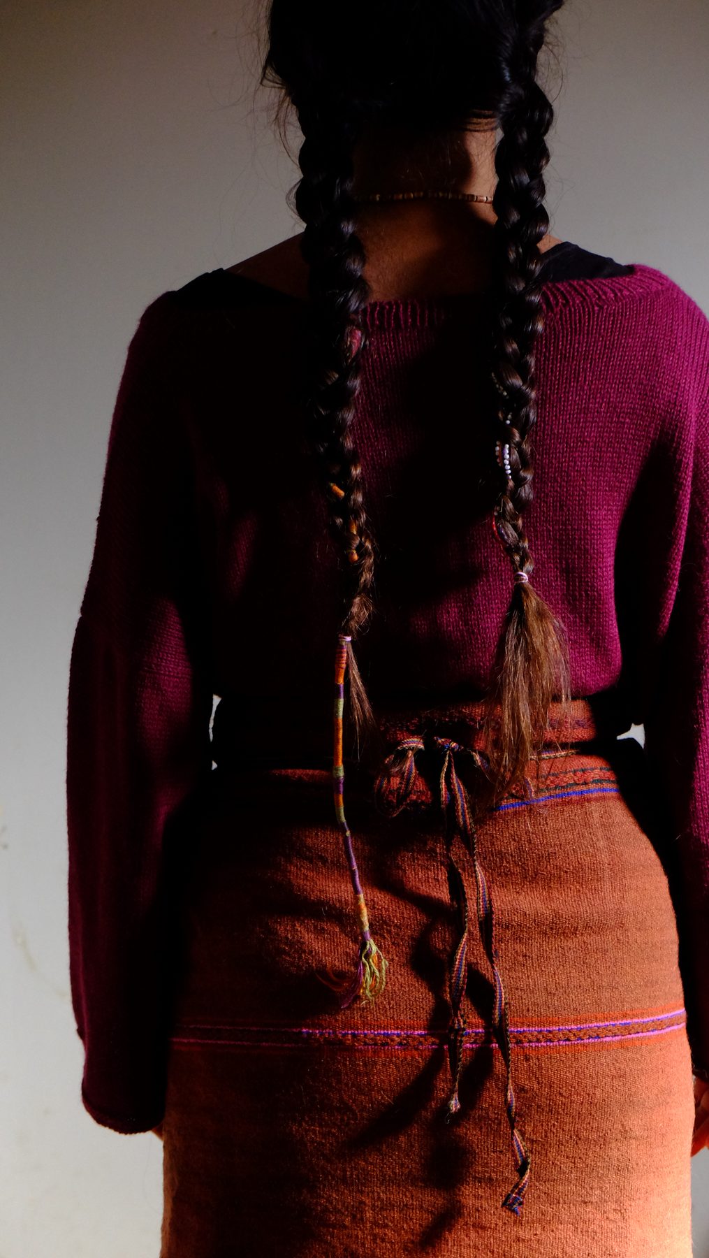 An antique handwoven skirt in deep terracotta, worn loose with a long braid