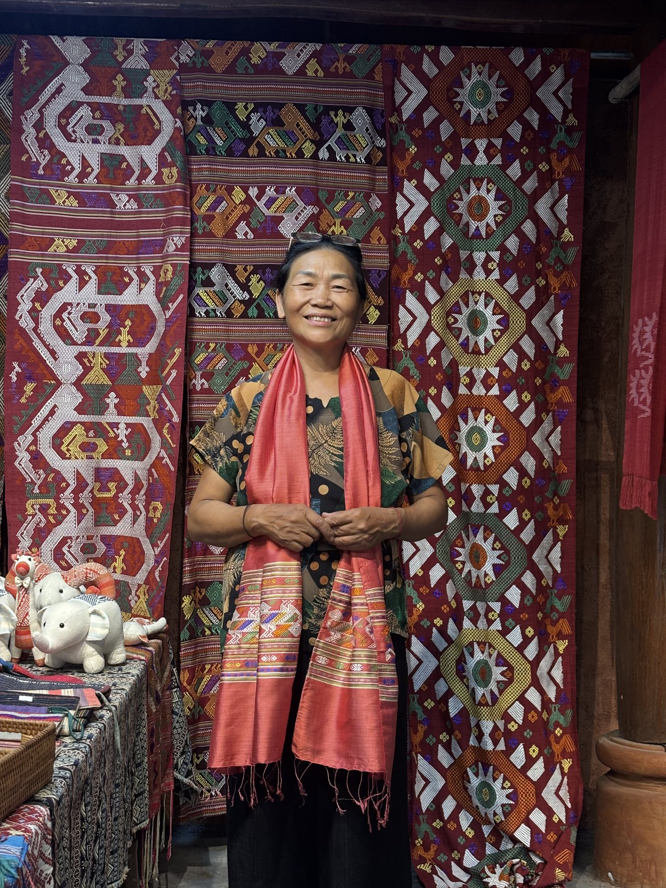 Cô Bích smiling in a woven scarf, in front of Thái brocade hangings