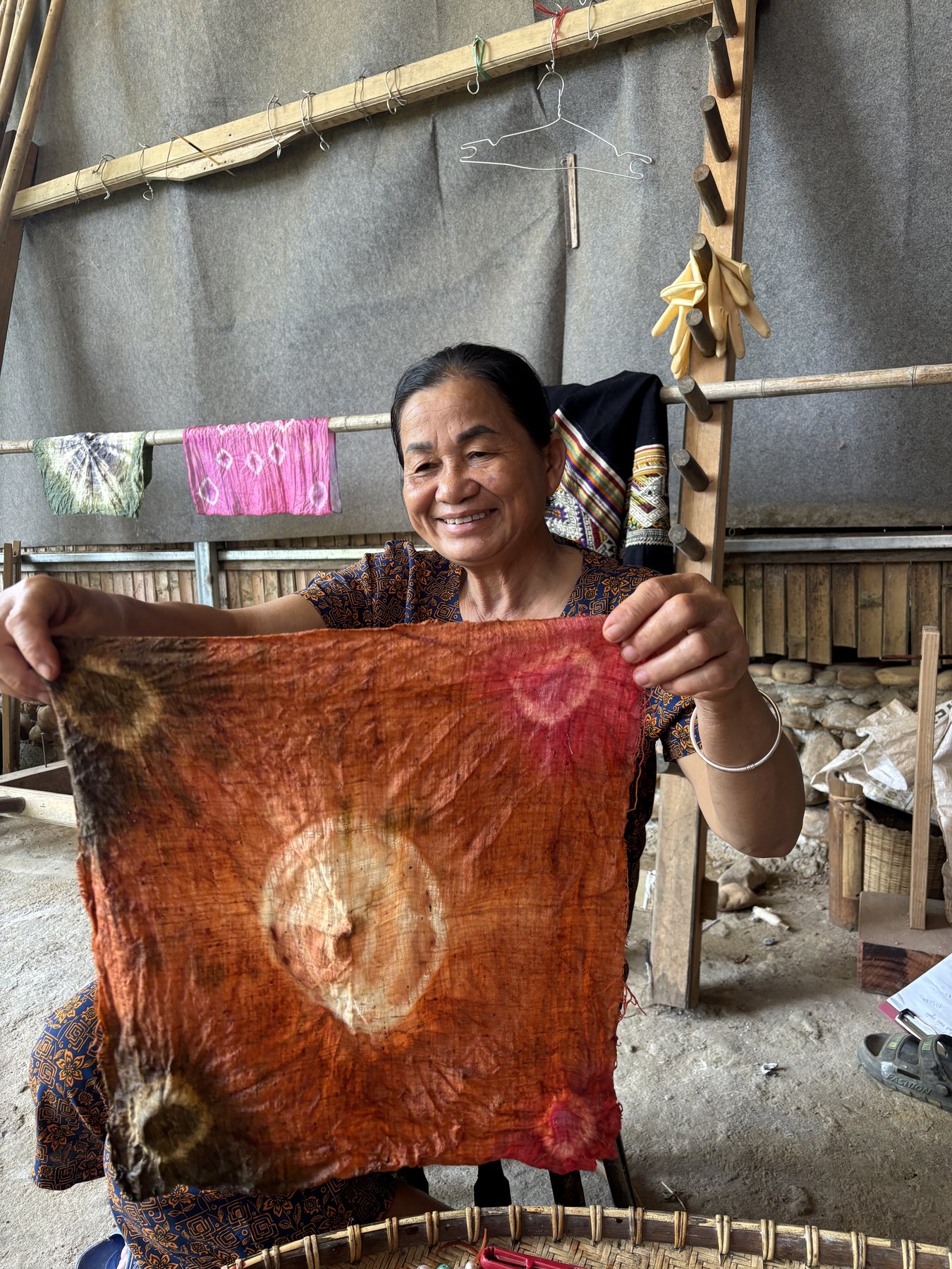 Cô Bích and Cô Hoa together, holding up a length of plant-dyed silk in warm rust and orange