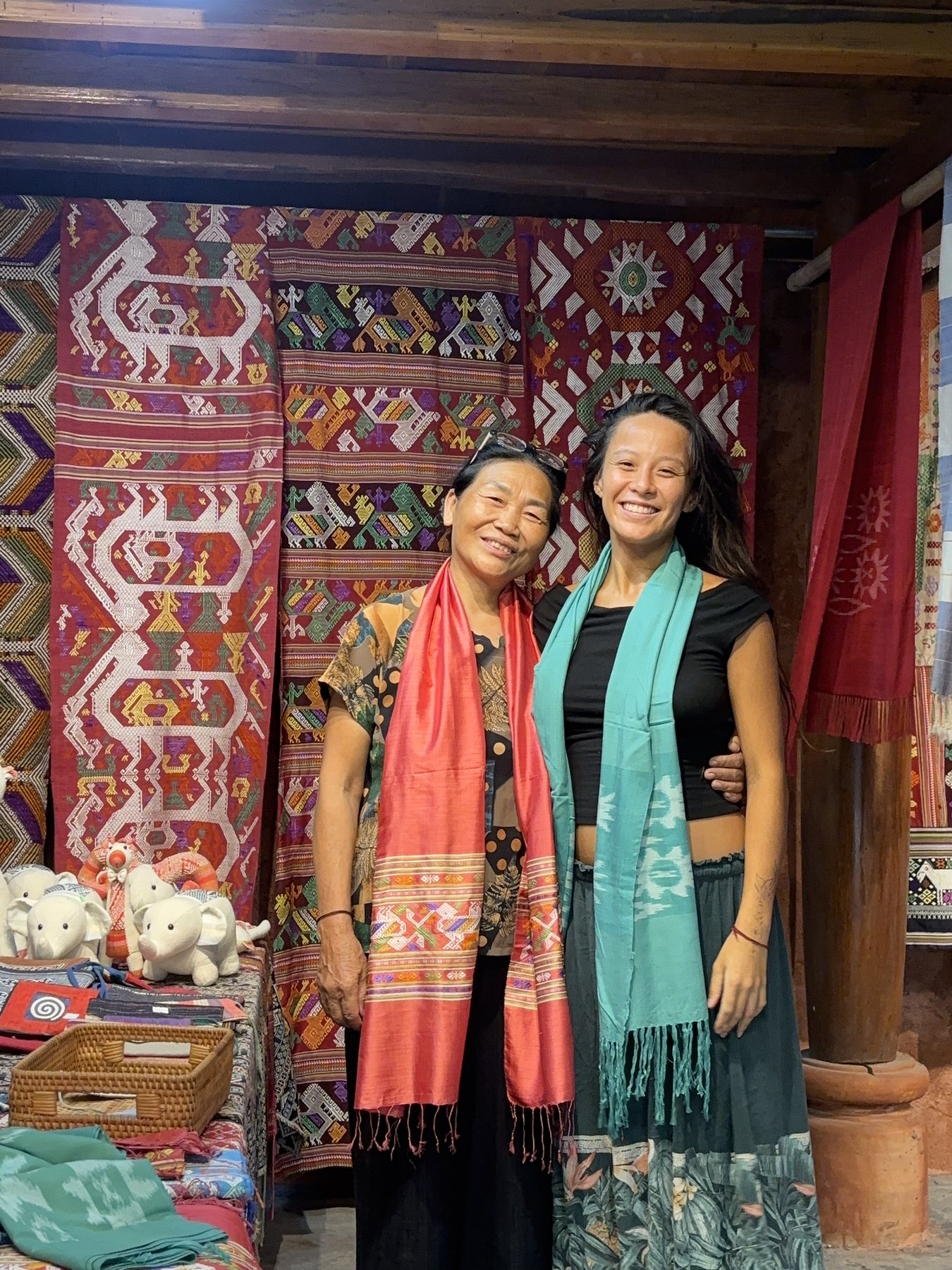 Cat-Vi and Cô Bích arm in arm, with textiles behind them